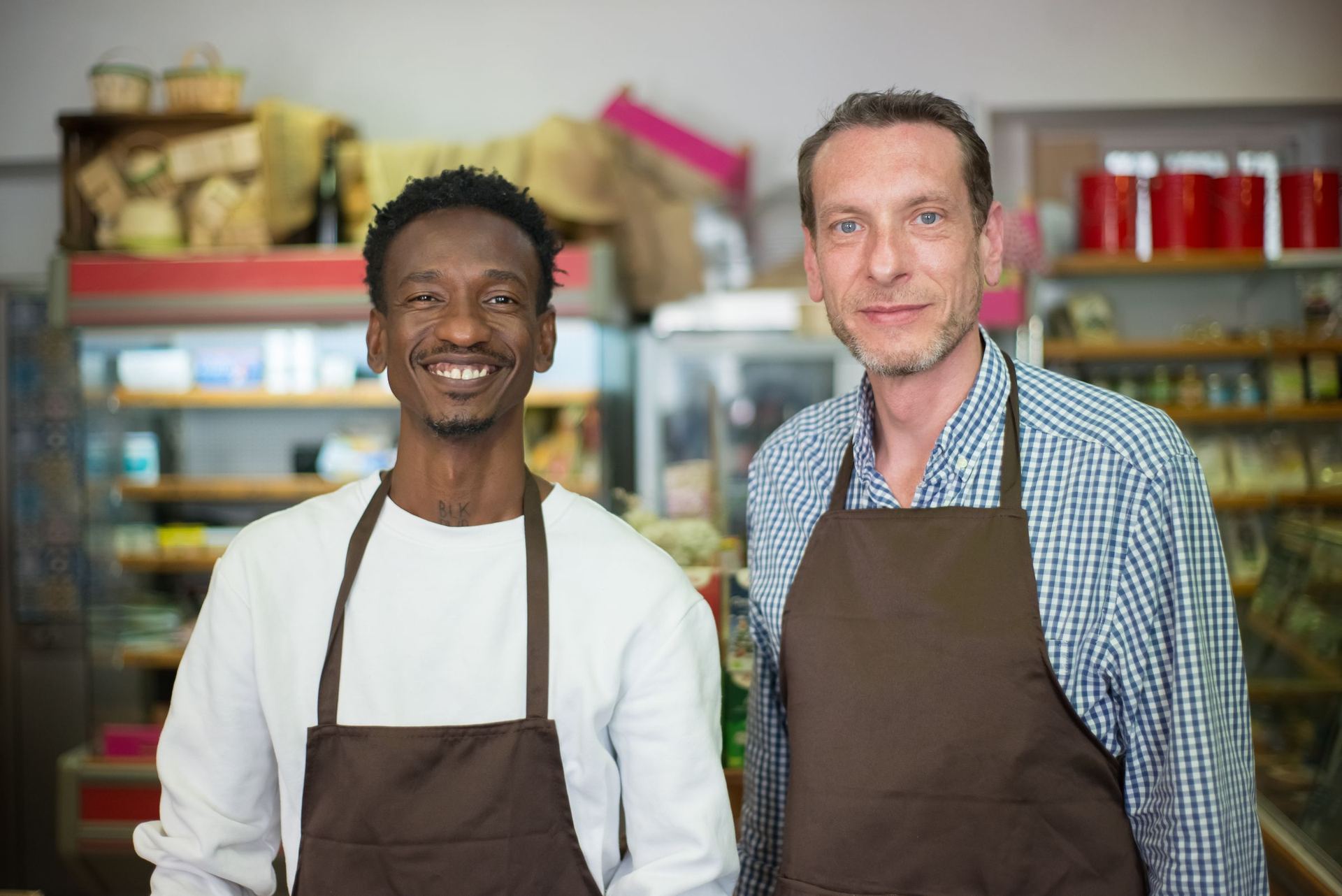 Two smiling owners of a local grocery store, in aprons, in their shop